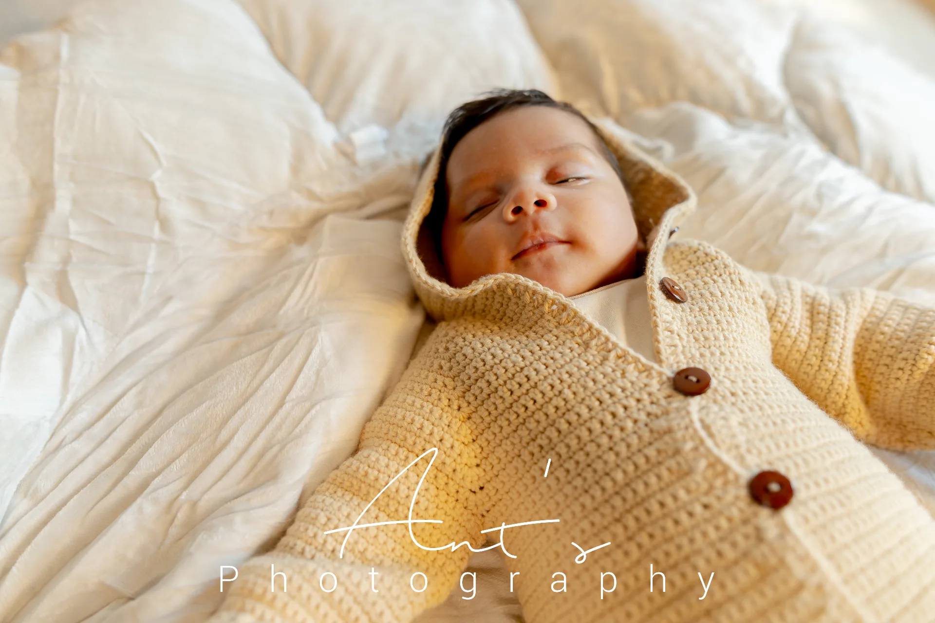 Cairo sleeping peacefully on white bedding in a cream knitted outfit
