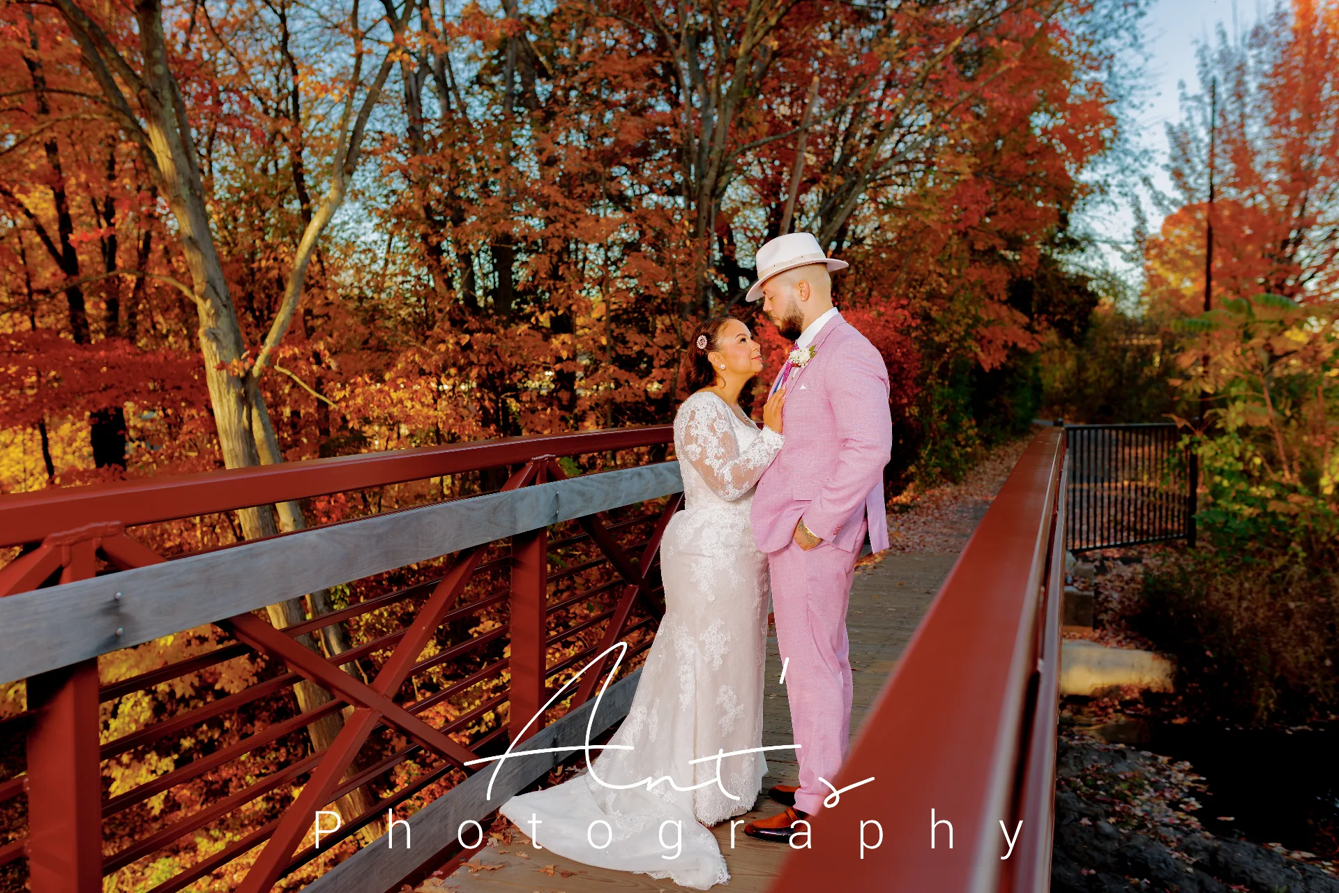 Bride looking up at the groom in a white hat on a bridge surrounded by orange autumn leaves